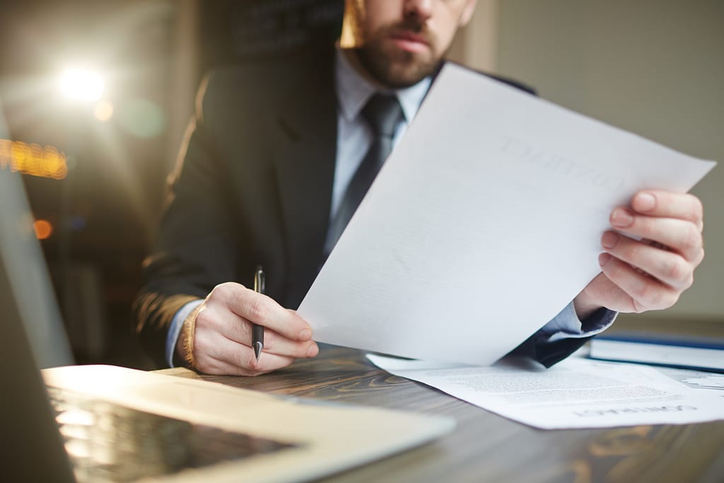 A bearded man in a suit holding a pen, checking over a Will for Free Wills Month.