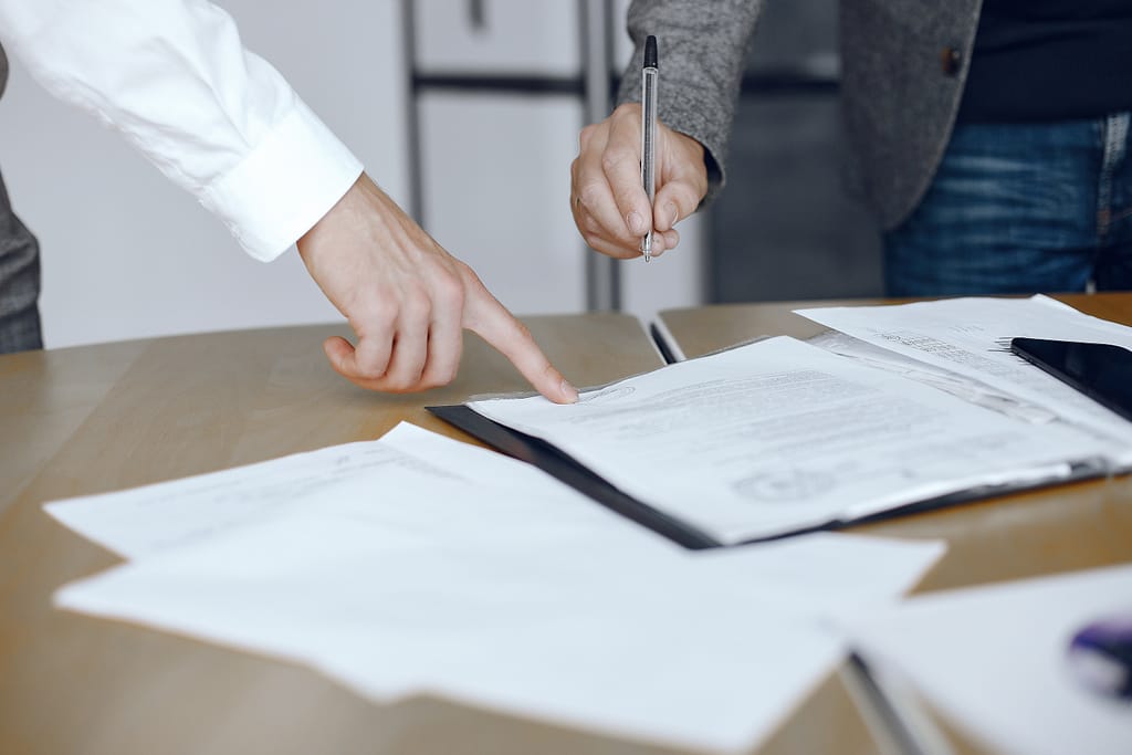 Two people looking at a contract discussing what you should never put in a Will. One man is pointing at the contract, the other is holding a pen about to sign it.