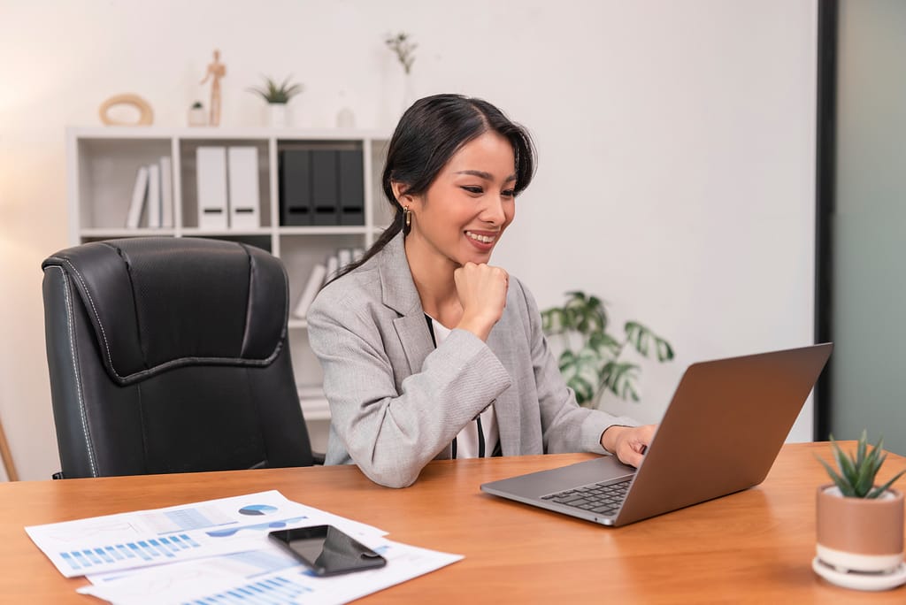 A woman in a suit smiling at a laptop.