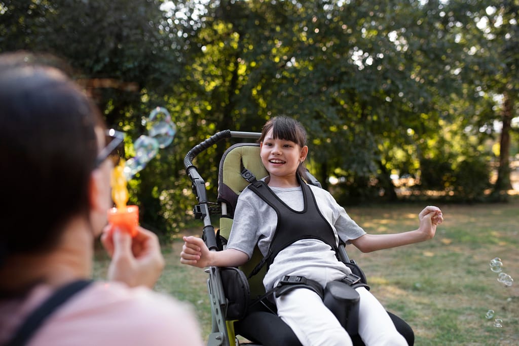 A young girl, with special needs, watching excitedly as her mother blows bubbles. She is strapped into a wheelchair - for the vulnerable person's trust blog.