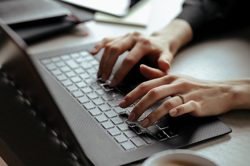 A picture of a woman's hands as she types on a laptop. She is looking up her digital assets. 
